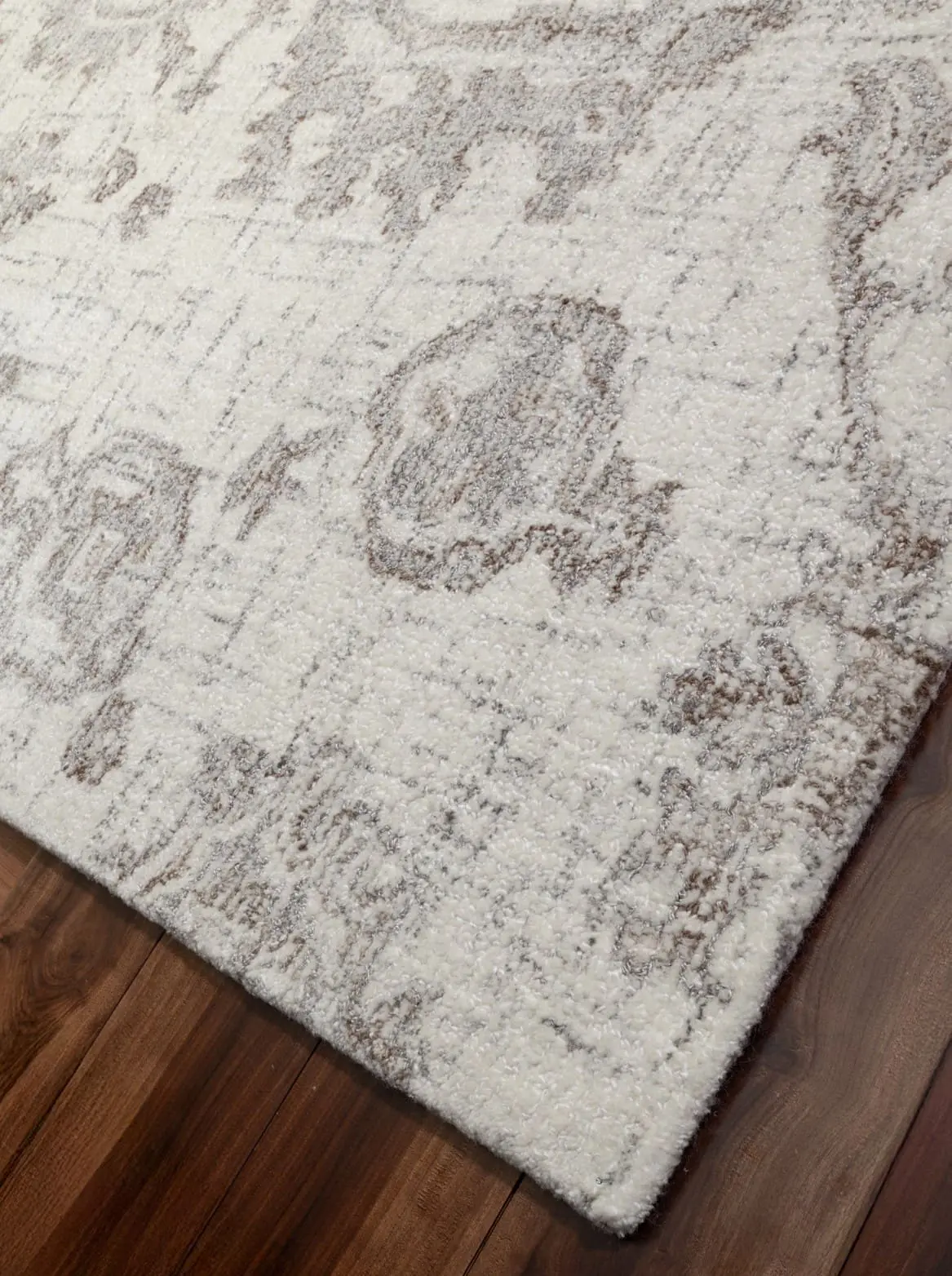 Close-up of a light cream rug with a subtle gray pattern on a wooden floor.