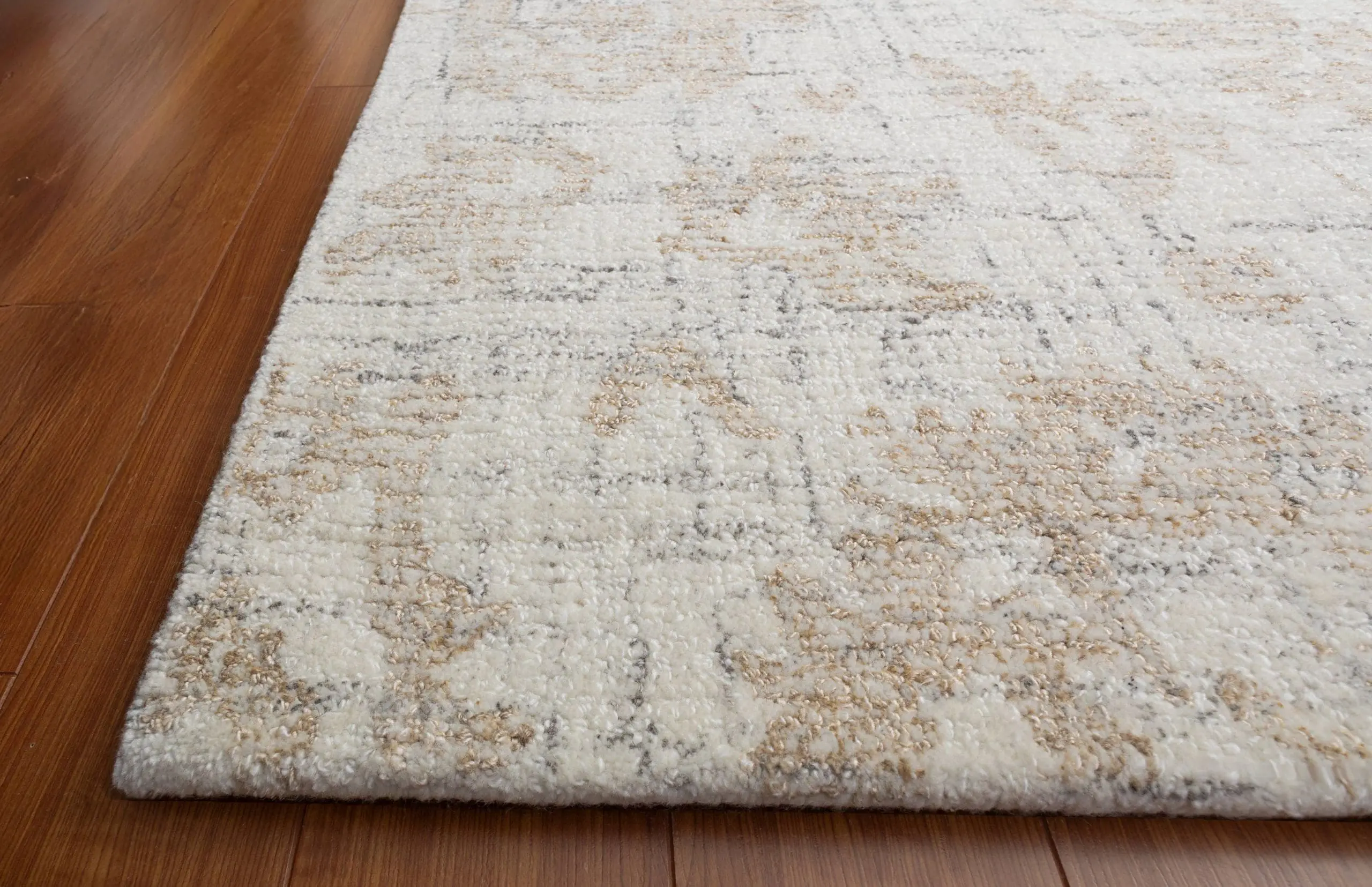 Close-up of a light patterned area rug resting on a dark wood floor, showing the rug edge where it meets the floor.