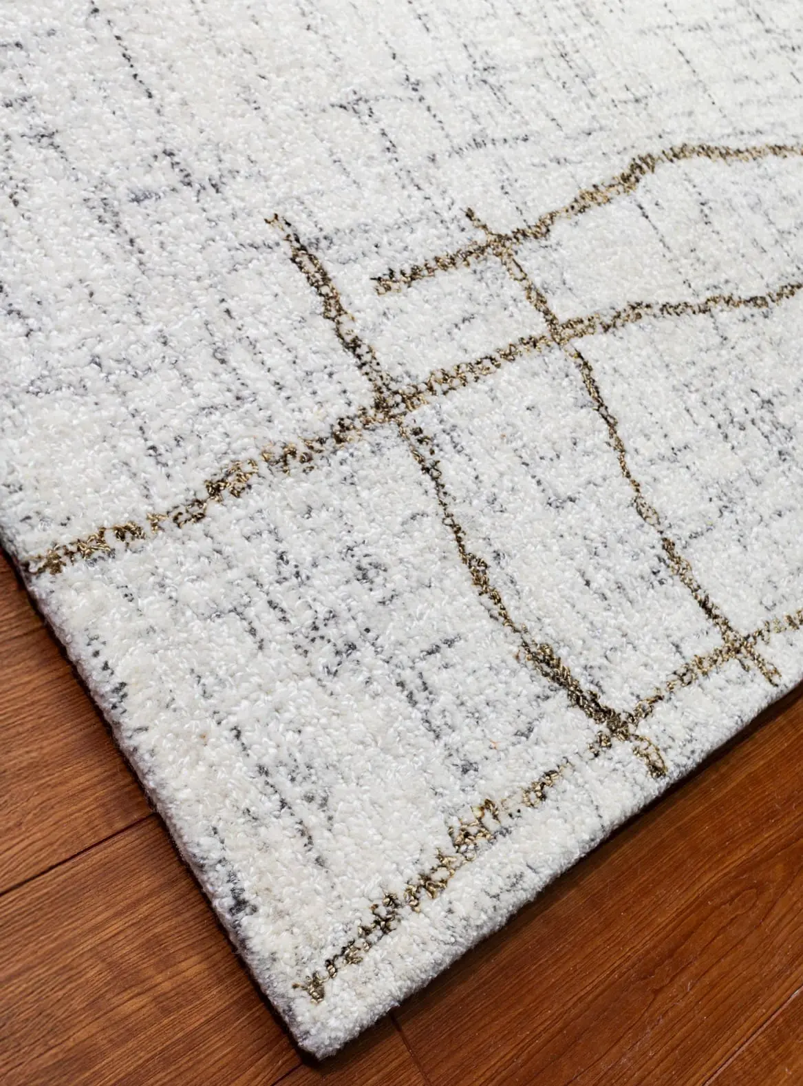 Light gray area rug with a subtle brown grid pattern on a wooden floor edge.