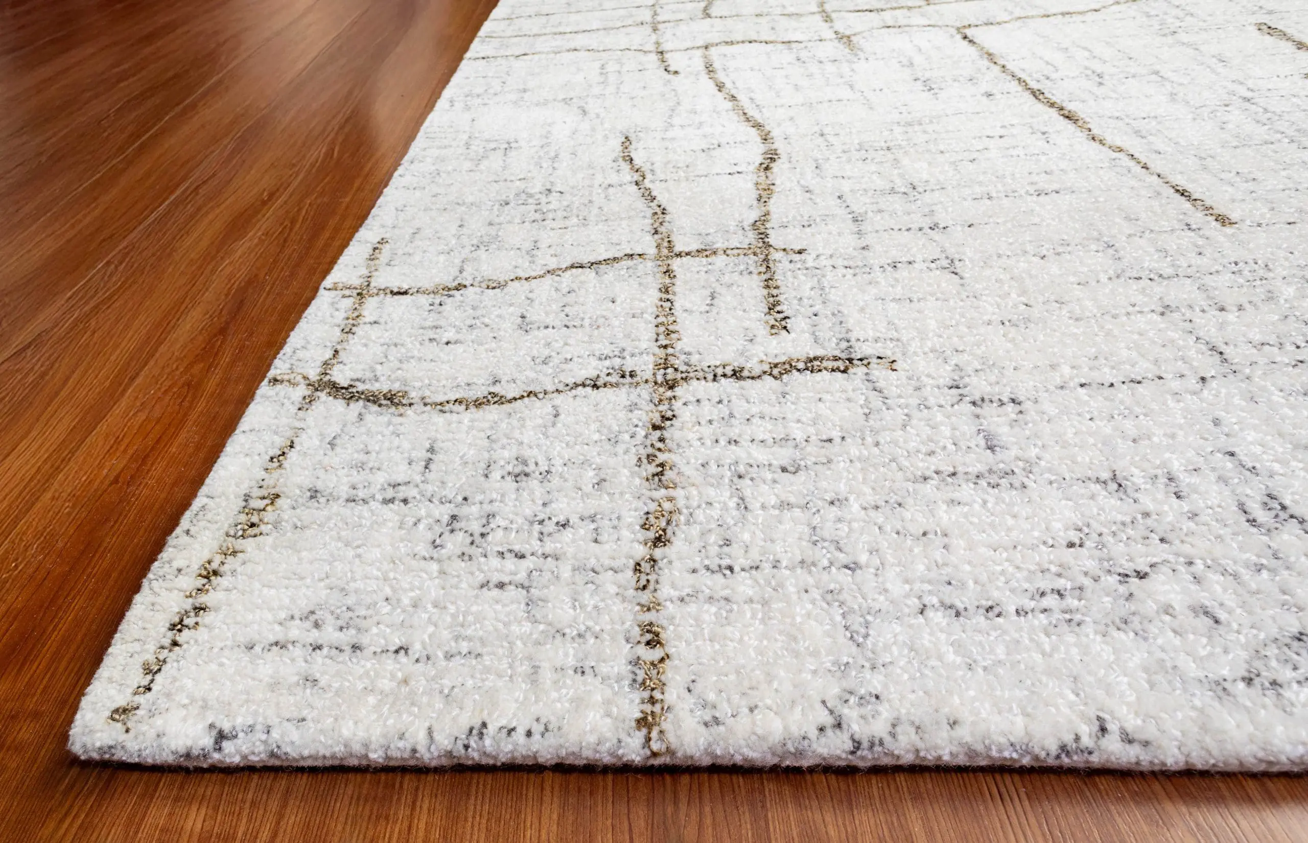 Edge of a white textured area rug with brown grid-like lines resting on a wooden floor.