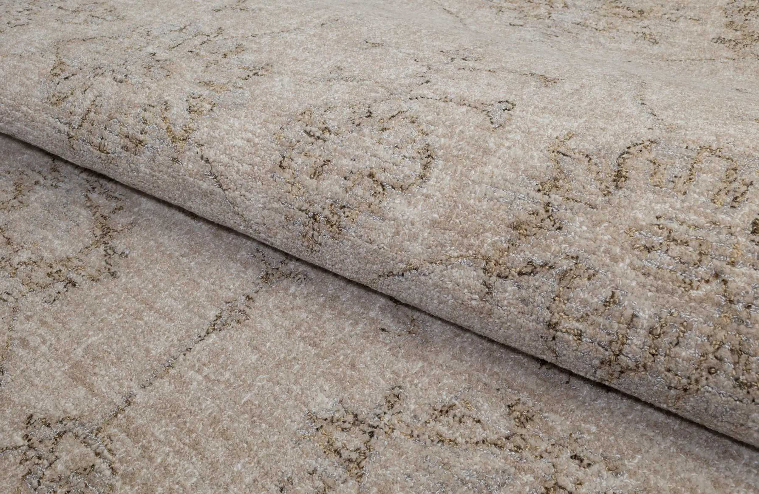 Close-up of a plush beige carpet with a subtle dark brown geometric pattern and rolled edge nearby.