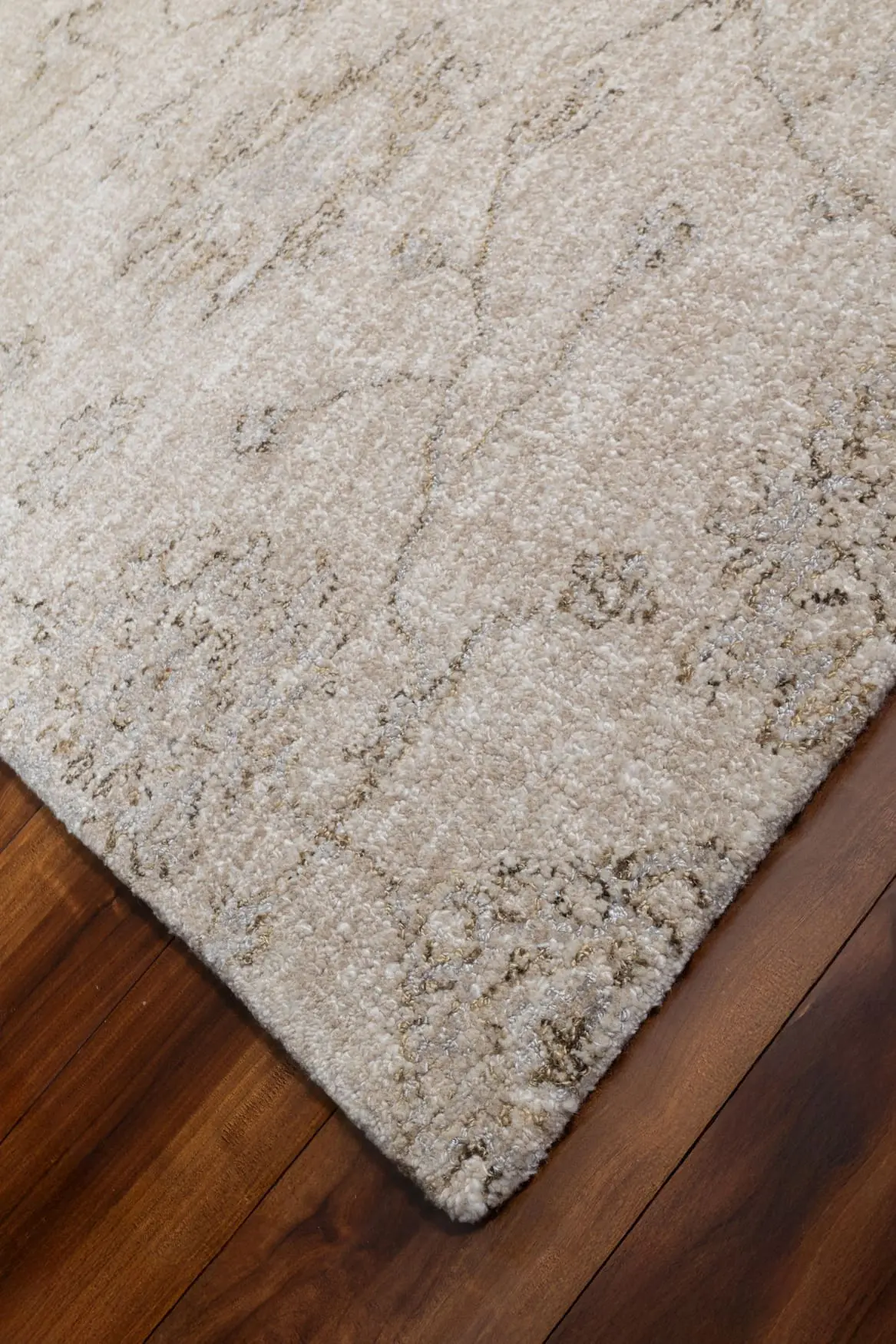 Beige patterned area rug on a dark wood floor, showing a soft, fluffy texture and subtle gray veining.