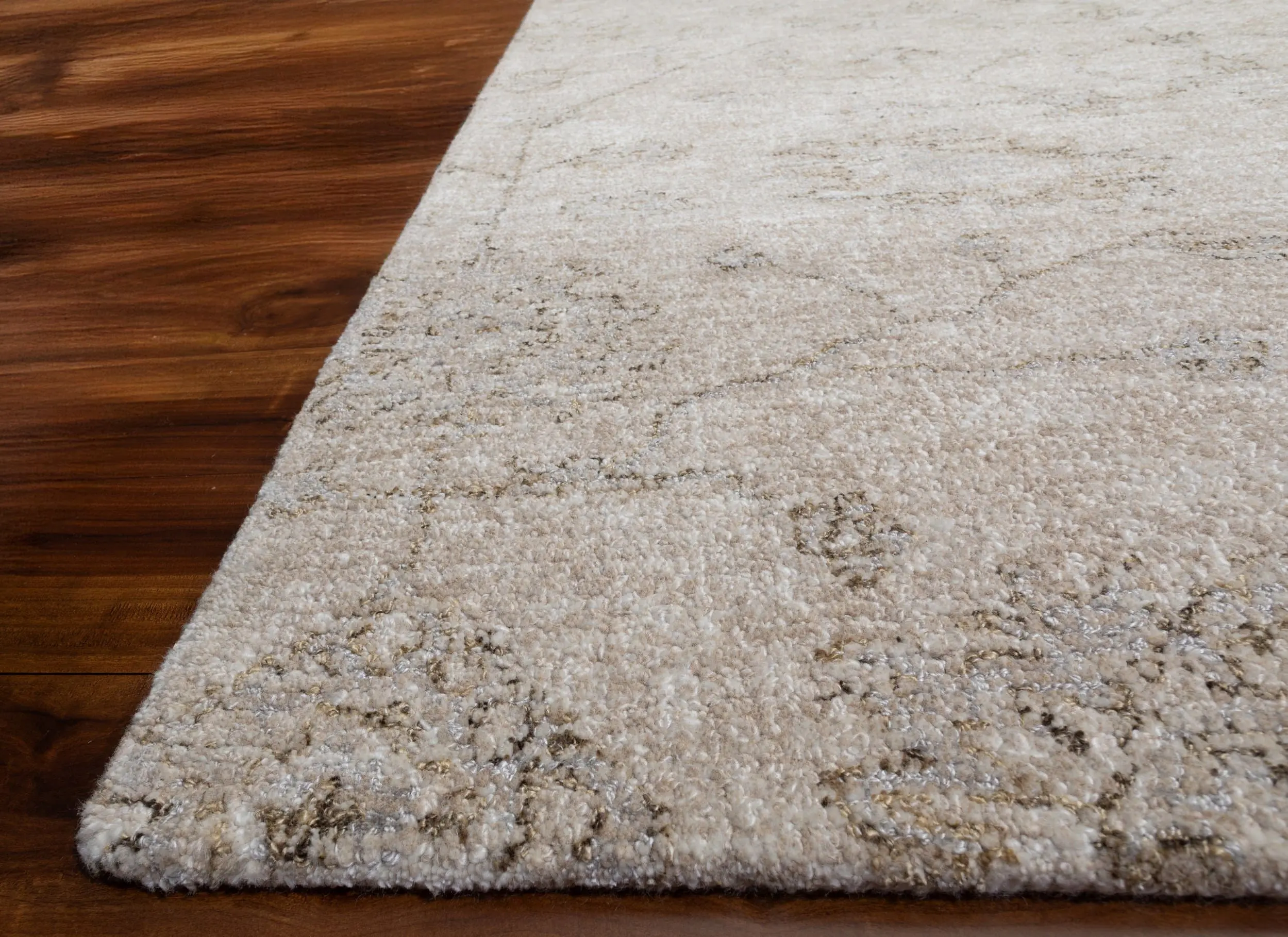 Close-up of a light beige textured rug edge where it meets a dark hardwood floor.