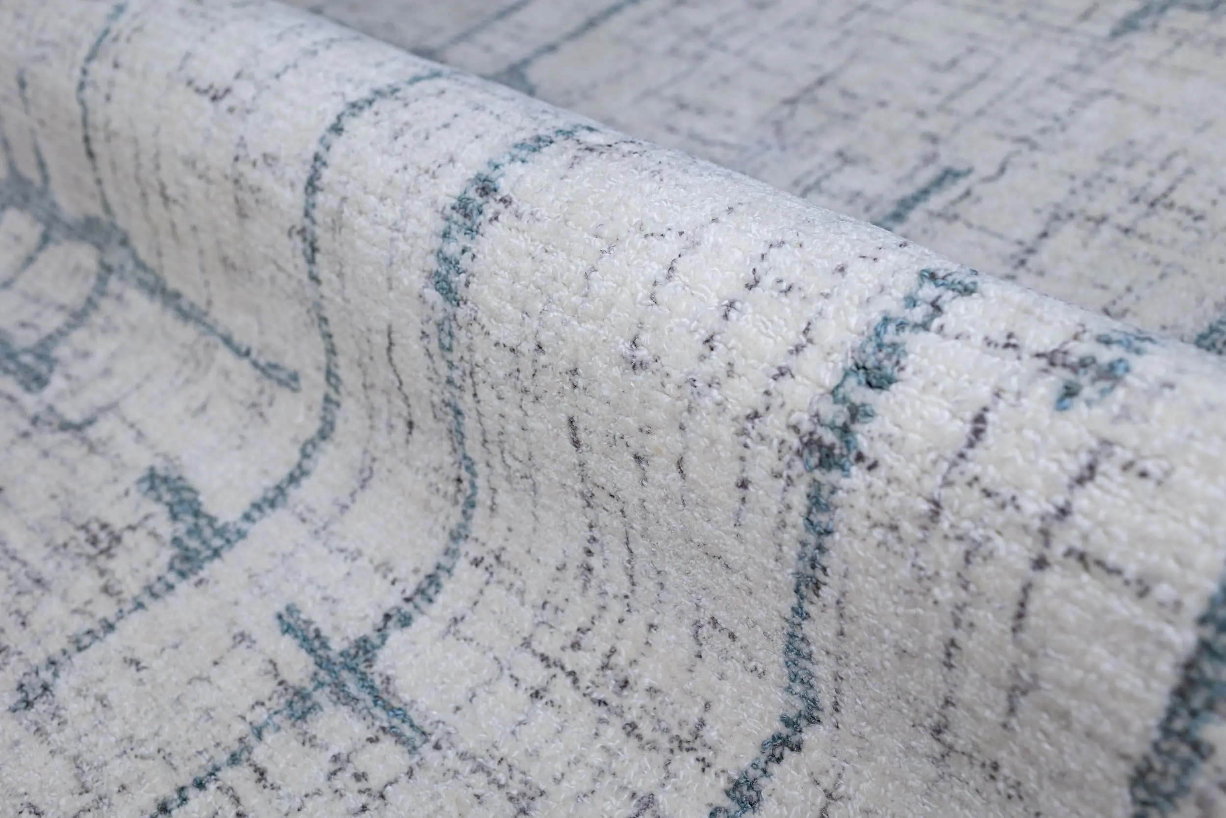 Close-up of a cream-colored textured rug with a blue-gray, curved line pattern for decorative detailing.