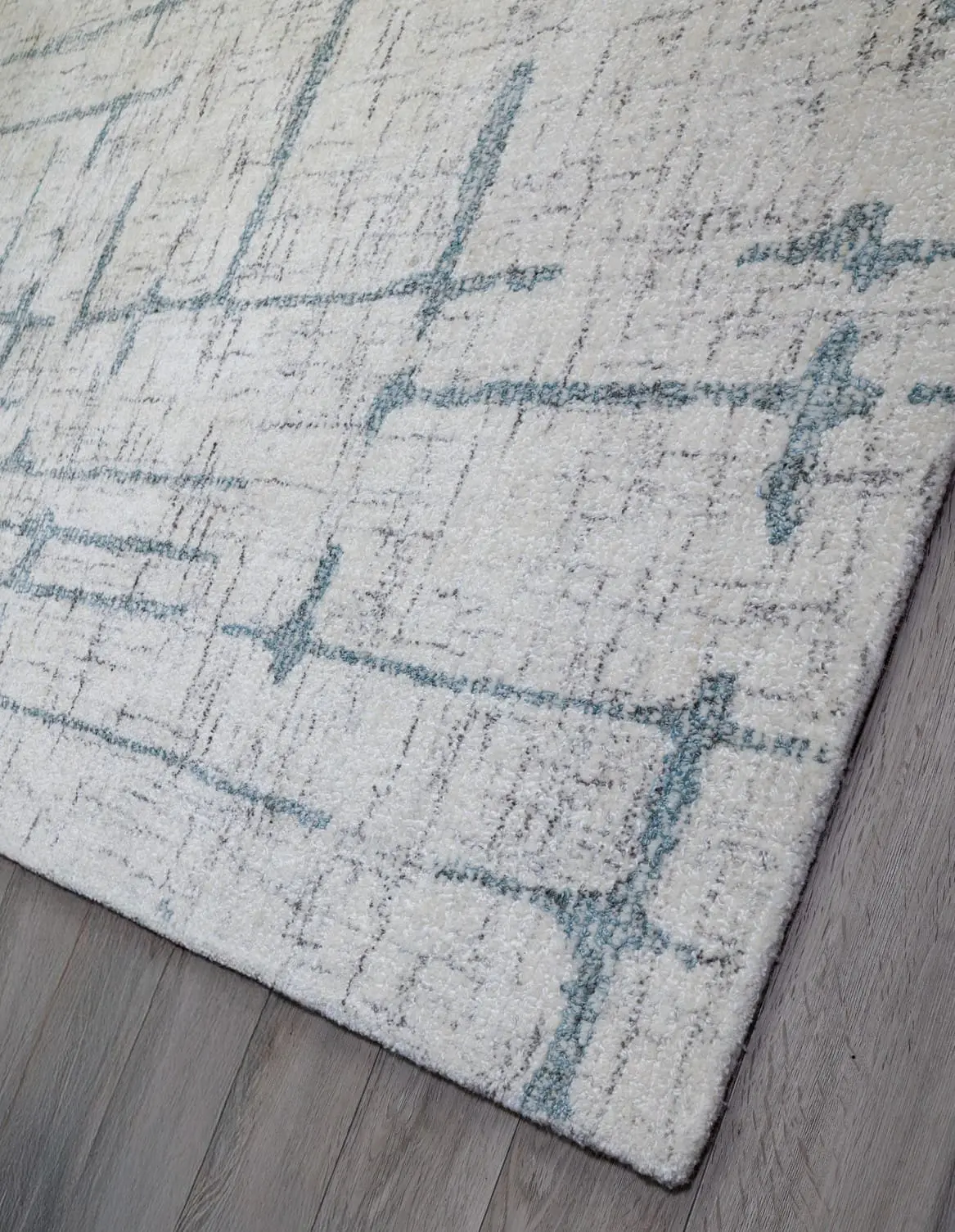 Cream area rug with blue geometric lines laid on a light wood floor, angled in the room.