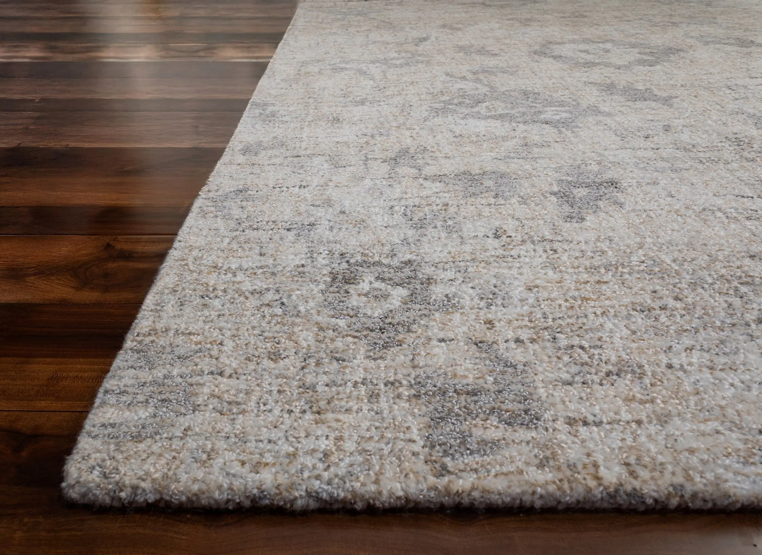 Beige and gray patterned area rug laid over dark hardwood floor.