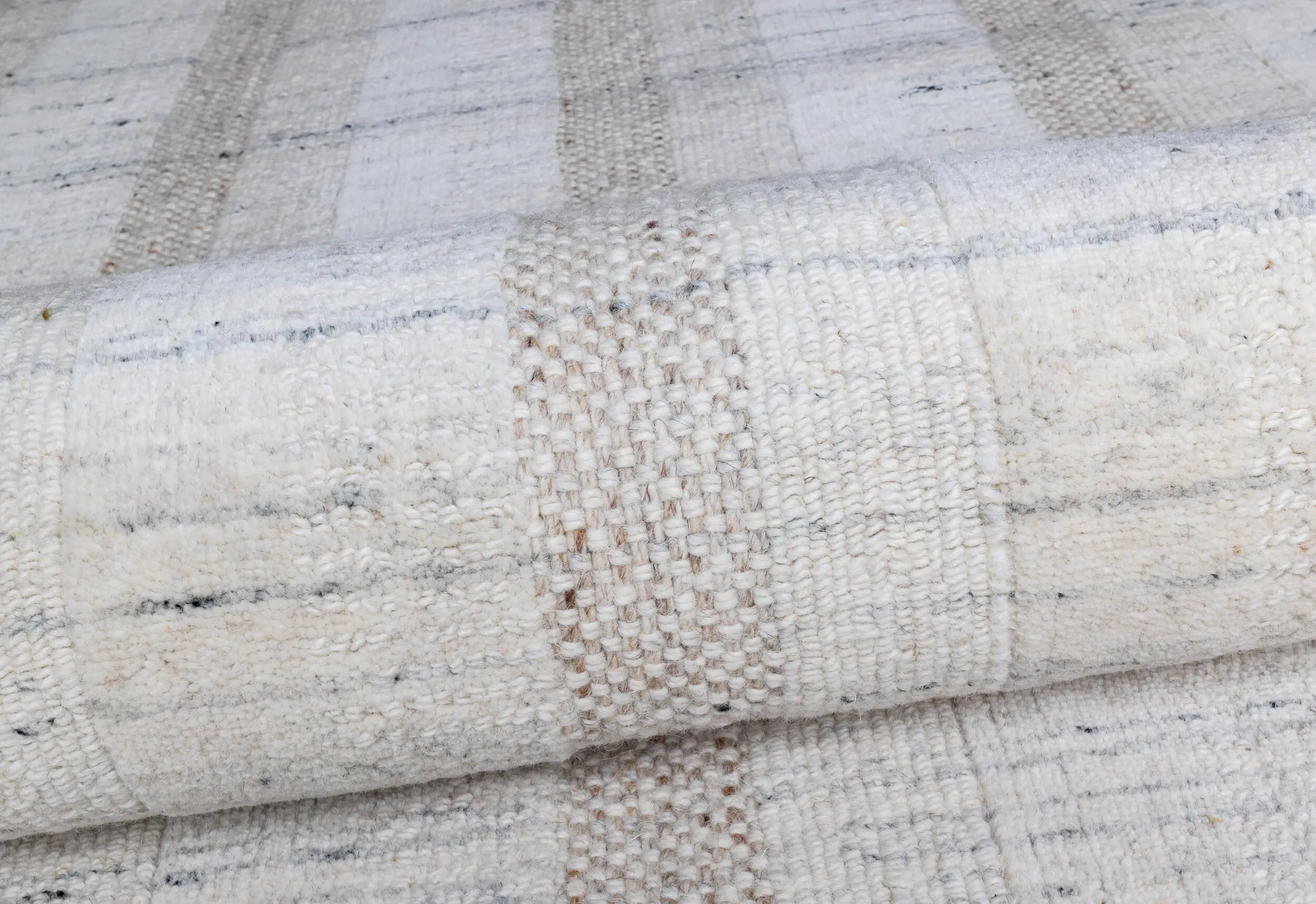 Close-up of a light cream woven rug showing textured loops and subtle striped pattern in beige and gray tones.