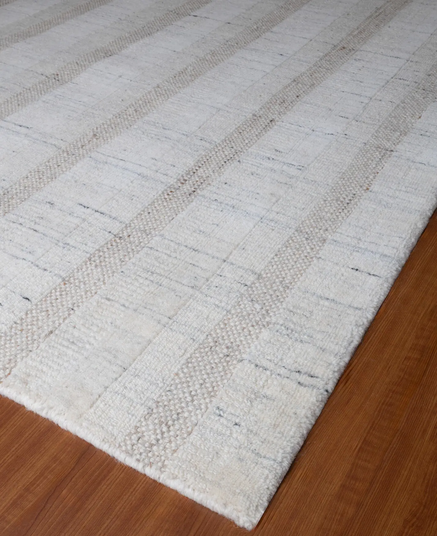 Cream-colored area rug with beige stripes on a wooden floor, corner visible.